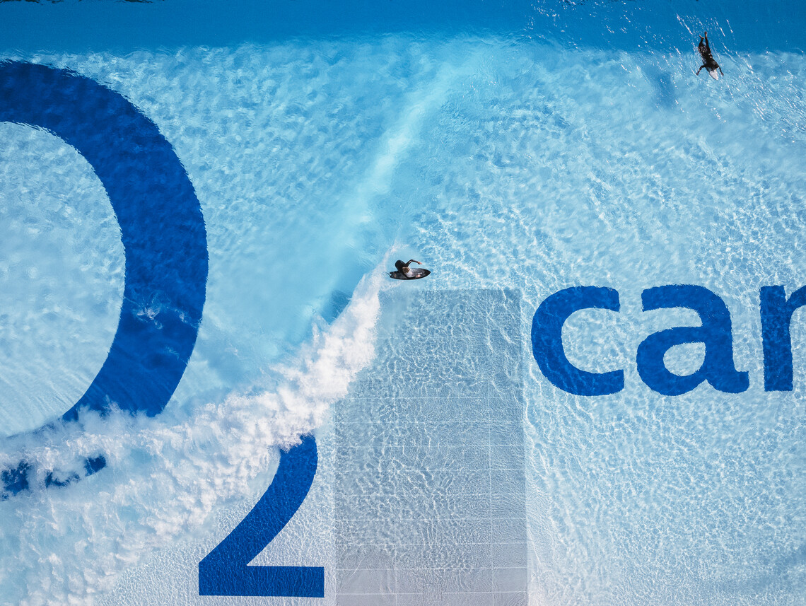 Der perfekte Moment für jeden Surfer: Das Bild zeigt aus der senkrechten Draufsicht einen seitlich hereinrollenden Wellekamm und einen Surfer, der gerade im Begriff ist sich aufzurichten um die Welle zu surfen, während die Lip kurz davor steht sein Board zu erreichen.